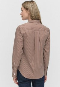 Chemise à manches longues rayée marron et crème avec un col, des poignets à bouton et un ourlet légèrement arrondi. Présente un petit logo au dos.