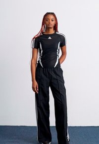 Black athletic outfit featuring a fitted short-sleeve top with white accents and loose-fitting pants with side stripes.