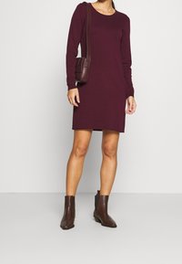 Burgundy långärmad klänning med rund halsringning, kombinerad med mörkbruna texturerade ankelstövlar och en matchande axelväska.