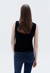 Top in maglia nera senza maniche con scollatura tonda, abbinato a jeans attillati blu scuro con tasche posteriori e leggeri dettagli di cucitura.
