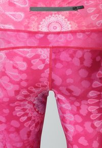 Leggings rosa con un audace motivo astratto multicolore caratterizzato da design floreali e a goccia. Il materiale sembra elastico e presenta una tasca con zip sicura.