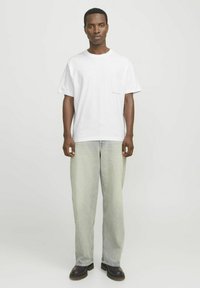 Weißes Baumwoll-T-Shirt mit Rundhalsausschnitt, kurzen Ärmeln und einem kleinen roten Logodetail. Kombiniert mit lockeren, hellen Denim-Jeans und dunklen Stiefeln.