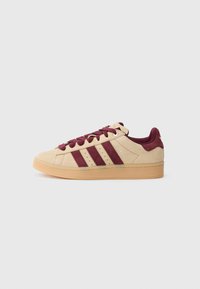 Bēša zamšādas sporta apavu ar bordo svītrām, šņorēm un papēža detaļu, gumijas zolīte un "Campus" etiķete sānos, redzams no ārpuses.