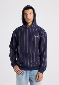 Laivaston huppari, jossa on pystyssä olevia punaisia ja valkoisia raidallisia kuvioita. Varustettu kengurupussilla ja brodeeratulla logolla. Valmistettu pehmeästä materiaalista; rento istuvuus.