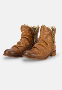 Botas de cuero marrón hasta el tobillo con un diseño arrugado, detalles de cremallera dorada y textura punteada. Suelas planas y punteras redondas.