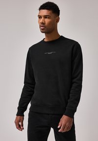 Sort crewneck sweatshirt lavet af blødt stof, med et lille hvidt logo på brystet. Klassisk pasform med ribbede mansjetter og kant.