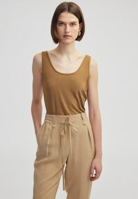 Top con scollatura a barca di colore marrone abbinato a pantaloni beige larghi con vita elastica e dettagli con bottoni.