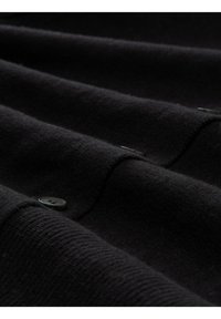 Nahaufnahme von schwarzem Wollstoff mit sichtbaren Nähten und einem einzelnen schwarzen Knopf, der die Textur und Details des Kleidungsstücks hervorhebt.