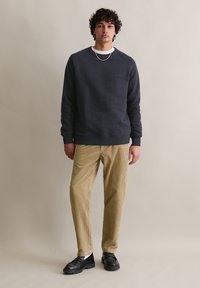 Felpa girocollo grigio scuro con polsini a coste, abbinata a pantaloni in corduroy beige con righe verticali, completata da scarpe nere.