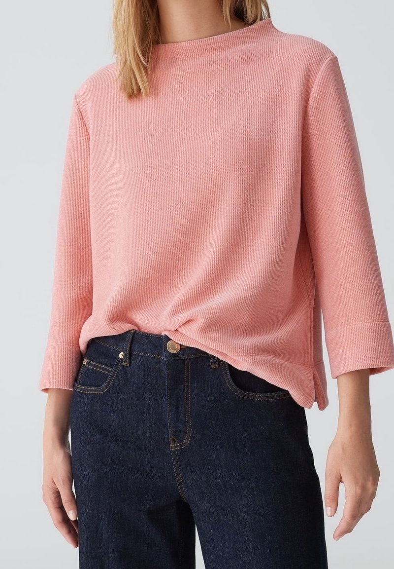 Personne portant un haut à manches longues côtelé rose clair et un jean bleu foncé, avec le haut légèrement rentré à l'avant.