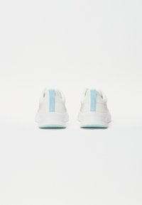 Baskets blanches avec un design texturé, dotées d'une languette de talon bleu clair et d'une semelle extérieure vert menthe. Style minimaliste, vue arrière.