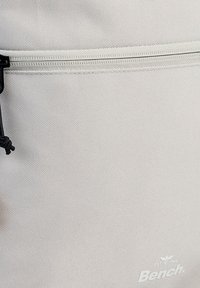 Grijze textielen rugzak met een glad oppervlak, gevlochten zwarte trekkoord en witte logo-details in de onderste hoek.