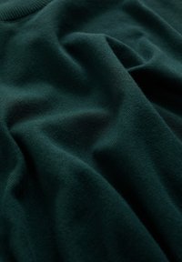 Mjuk, mörkgrön stickad tyg med synlig struktur och mjuka veck.