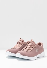 Světle růžové sportovní boty vyrobené z prodyšného materiálu, s designem na šněrování, polstrovanou podrážkou a decentním logem na boku.