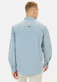 Lichtblauw overhemd met lange mouwen in een gladde stof. Voorzien van een button-down kraag, knoopmanchetten en een gestikte accent achterop.