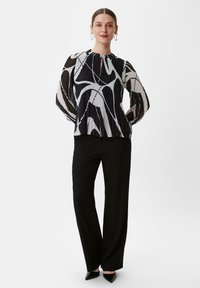 Czarna i biała plisowana bluzka z długimi rękawami i dekoltem w kształcie łezki, zestawiona z czarnymi szerokimi spodniami i czarnymi szpilkami.