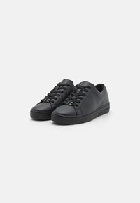 Mustad mustad sneakerid, millel on sile viimistlus, ümar varvas, lame must tald ja mustad paelad. Sisaldab õrna brändimist kanna lähedal.