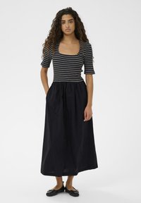 Črtasta črno-bela oprijeta majica s kvadratnim izrezom, ki prehaja v tekočo črno krilo. Ima kratke rokave in stranske žepe.