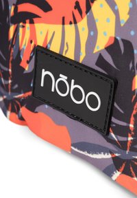 Monivärinen kangaslaukkussa on trooppisen lehden kuvio, ja siinä on musta suorakaiteen muotoinen logotarra, jossa lukee "nōbo" valkoisella. Sujuva pinta.