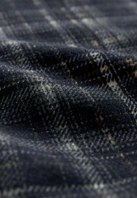 Vlněná kostkovaná látka s tmavě námořnickým základem a světle šedými a hořčicově žlutými protínajícími se liniemi, představující měkký, texturovaný povrch.