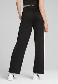 Mustad lai jalad, mis on valmistatud sileda kangast, sisaldavad elastset vöökohta ja kontrastset valget külgtriipu. Koos valgete tennisetossudega.