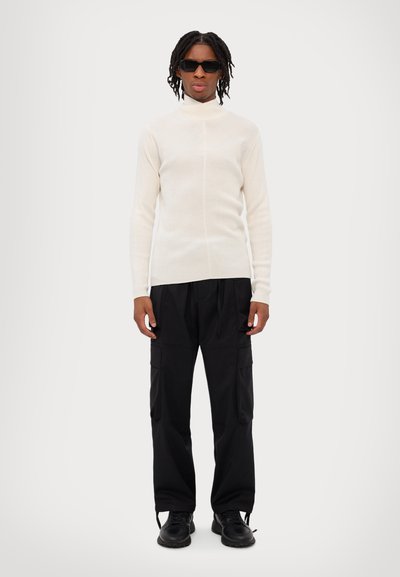 Kremfarvet ribbet polo sweater sat sammen med sorte cargo bukser. Sorte solbriller og klodsede sorte sko fuldender looket.