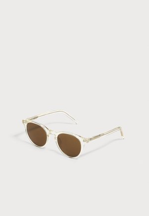 Clear frame sunglasses with round brown lenses resting on a white surface, shown at a slight angle.
