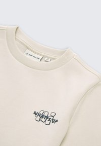 Lichtbeige sweatshirt met ribbelboord, voorzien van de tekst "WHAT'S UP" in donkerblauw. Glad textuur, minimalistisch ontwerp, oversized pasvorm.