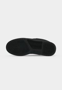 Semelle de chaussure noire avec motifs de bande de roulement texturés comprenant des rainures en zigzag et linéaires sur un fond blanc uni.