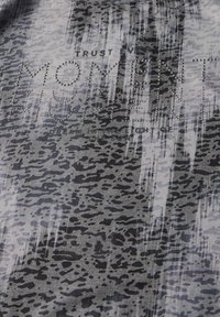 Tissu gris avec un motif animal texturé, orné de strass scintillants formant le mot "MOMENT" en lettres noires.