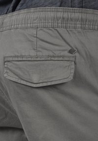 Gray shorts with a textured fabric, featuring a top-stitched back pocket and a small logo tag on the lower right corner.
