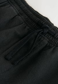 Gros plan d'une ceinture élastique noire avec un cordon noué sur un pantalon ou un short en tissu doux.