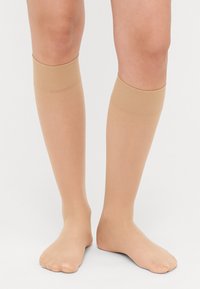 Nude kniekousen met een zachte, dunne textuur en geribbelde bovenbanden, ontworpen voor een comfortabele pasvorm. Open teenontwerp voor ademend vermogen.