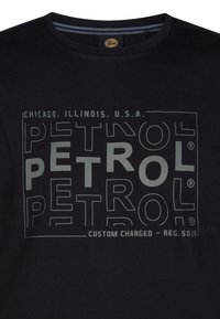 Černé bavlněné tričko s velkým grafickým potiskem, na kterém je nápis "PETROL" v různých velikostech a průhlednosti, spolu s textem "Chicago, Illinois, U.S.A.".