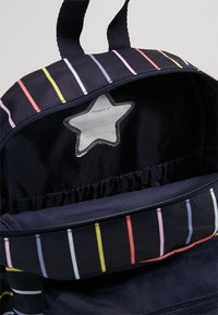 Mochila de tela azul marino con rayas horizontales de colores. El interior cuenta con un bolsillo con etiqueta en forma de estrella y almacenamiento elástico recogido.