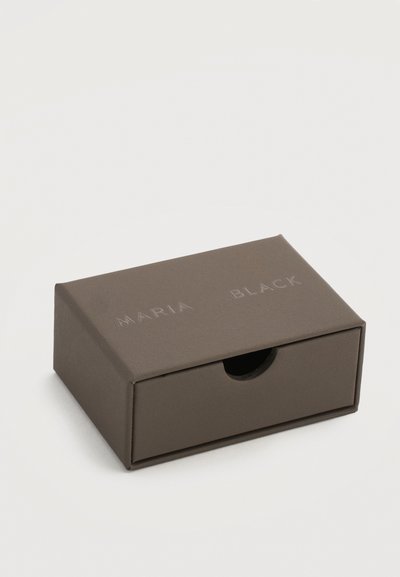 Μικρό κλειστό ορθογώνιο σκούρο γκρι κουτί με εμπρόσθιο συρτάρι και την εγχάρακτη επιγραφή "MARIA BLACK" στην επάνω επιφάνεια.