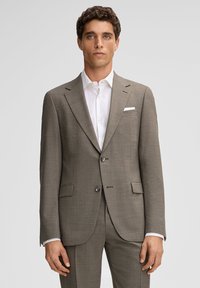 Brązowy teksturowany garnitur z klapą z nacięciem, dwoma guzikami i kieszeniami bocznymi. Połączony z białą koszulą i poszetką, prezentujący czysty, schludny design.