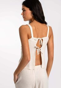 Top de lino color beige claro con tirantes gruesos, diseño de espalda descubierta atado con lazos y un corte relajado que llega hasta la cintura.