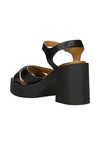 Černé platformové sandály s robustní podpatky, zakřivenými střihovými popruhy, hladkým koženým svrškem a tan insole. Design s otevřenou špičkou pro prodyšnost.
