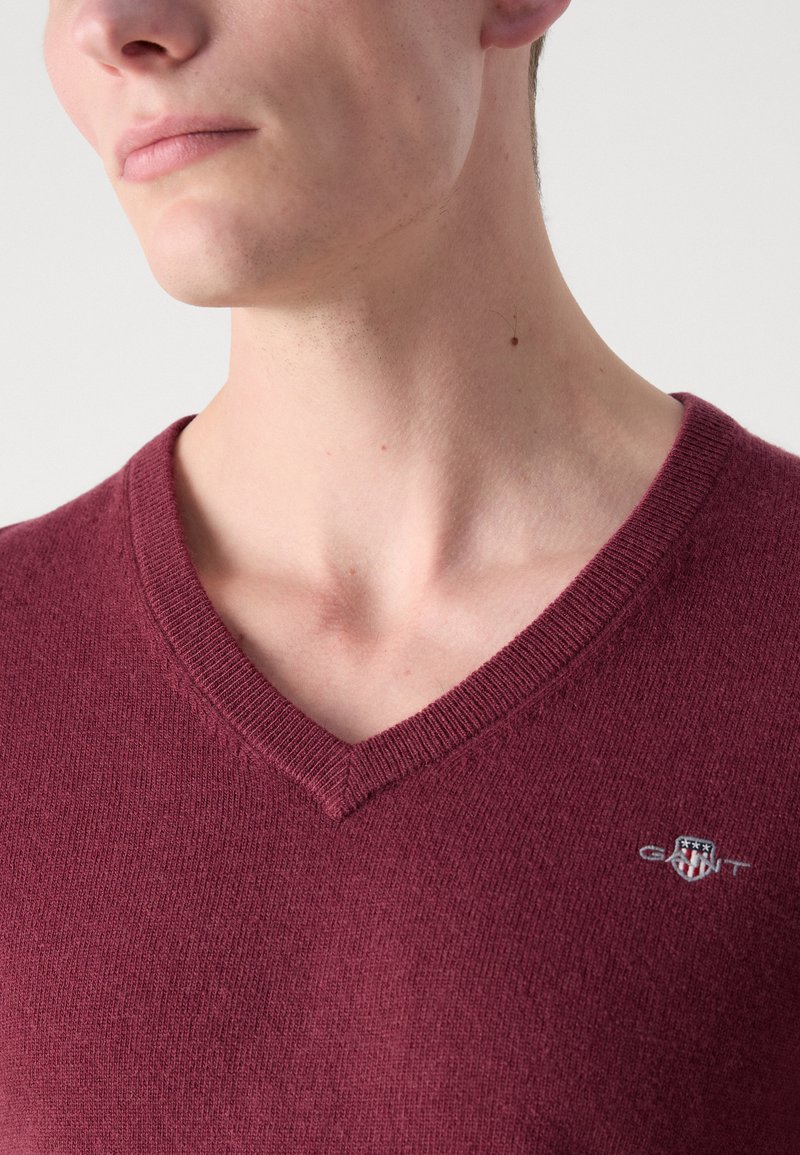 Suéter de punto suave en color burdeos con escote en forma de v, que presenta un cuello acanalado y un pequeño logotipo en el lado izquierdo del pecho.