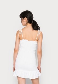 Vestido de verão branco com corpete franzido, alças ajustáveis e bainha em babados. O tecido texturizado acrescenta interesse visual ao design.