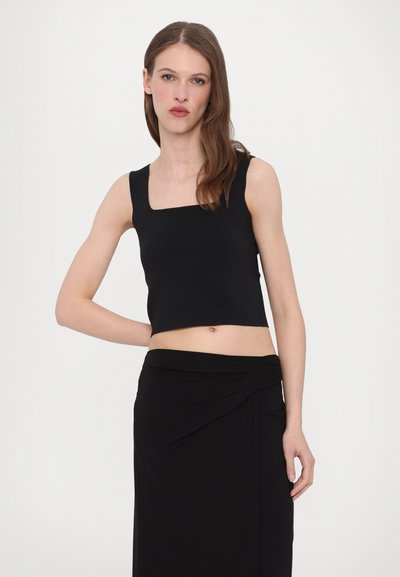 Black cropped tank top with a square neckline, made from smooth fabric, paired with a black wrap skirt showcasing a twisted detail.
