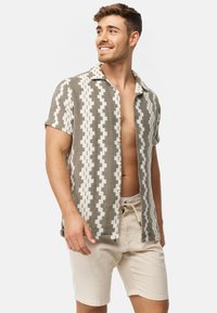 Chemise à manches courtes au motif en zigzag blanc et olive, faite d'un tissu texturé ; associée à un short beige clair.
