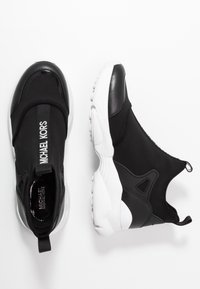 Czarne sportowe sneakersy z gładką cholewką, białą gumową podeszwą i detalem z logo. Posiadają elastyczny materiał i konstrukcję typu slip-on.
