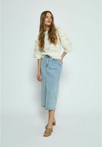 Witte gebreide trui met textuurstrepen, gecombineerd met een lichtblauwe denim rok en bruine block-heeled muiltjes. Eenvoudige, casual outfit.