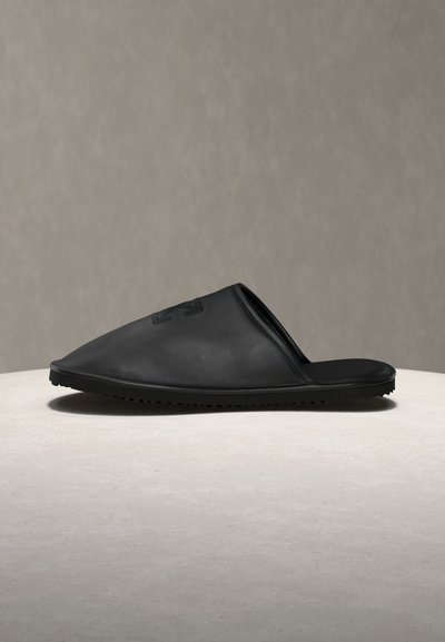 Μαύρο mule χωρίς λουράκια με κλειστή μυτερή μύτη και λεία επιφάνεια, τοποθετημένο σε ανοιχτή επιφάνεια σε ουδέτερο φόντο.