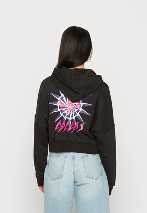 Sort cropped hoodie med et stort, farverigt grafisk design på ryggen, der fremhæver et stiliseret logo og pigge. Materialet ser blødt ud.