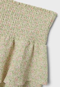 Abito floreale verde con corpino arricciato e orlo sfrangiato. Presenta un leggero motivo floreale in rosa e verde su uno sfondo chiaro.