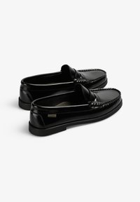 Par de mocasines negros de cuero con tacones bajos y detalles de costura, fotografiados sobre un fondo blanco.