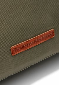 Khaki-Canvas-Produkt mit einem Lederpatch, auf dem "The Chesterfield Brand" steht. Es zeigt eine strukturierte Oberfläche und saubere Nähte.